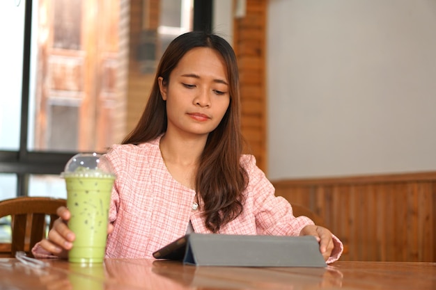 Azjatycka kobieta nawiasy klamrowe ogląda komputer Pij zieloną herbatę, aby się odświeżyć