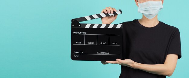 Azjatycka kobieta nosi maskę na twarz i trzymaj w ręku czarną deskę klapy lub używaj łupków filmowych w produkcji wideo, przemyśle kinowym na zielonej mięty lub Tiffany Blue tle.