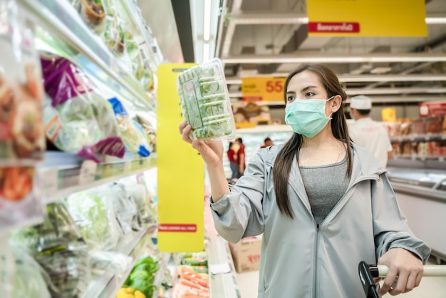 Zdjęcie azjatycka kobieta, nowy styl życia, zakupy w supermarkecie z ręką chroniącą maskę, wybierz świeże warzywa