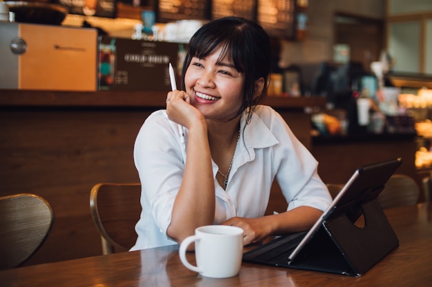 Azjatycka kobieta pije kawę w kawiarni i używa laptop dla pracować biznes