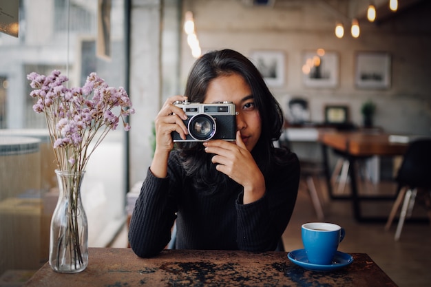 Azjatycka kobieta pije kawę w sklep z kawą kawiarni z rocznik kamerą