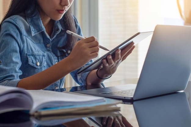 Azjatycka kobieta pisze na ekranie cyfrowego tabletu i pracuje na laptopie w domu