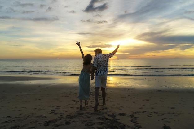 Azjatycka kobieta podróżnik trzymająca rękę mężczyzny i patrząca na piękny zachód słońca na plaży