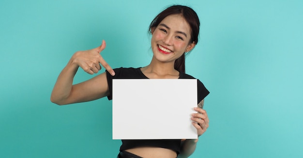 Azjatycka kobieta ręce trzyma pustą deskę z uśmiechniętą twarzą na miętowym zielonym tle. Pusty biały papier A4.