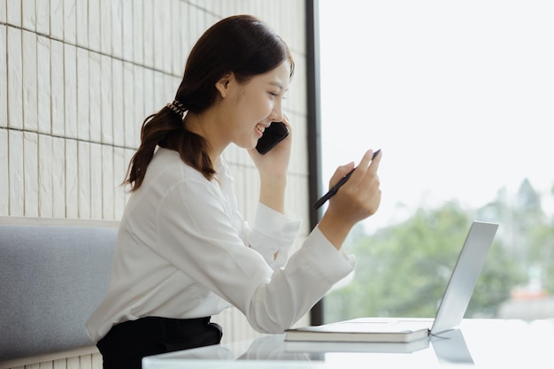 Azjatycka kobieta rozmawia przez telefon na kanapie w swoim gabinecie młoda bizneswoman założycielka firmy startowej prowadzącej biznes przez młode kierownictwo koncepcja biznesowa i prowadzona przez szefową