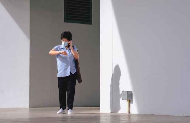 Azjatycka kobieta rozmawiająca na smartfonie i patrząca na zegarek, wychodząc z biura po pracy