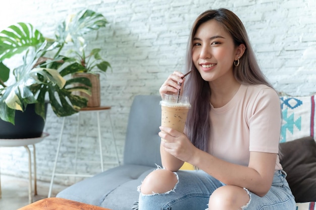 Azjatycka kobieta siedzi i pije mrożoną kawę i uśmiecha się radośnie