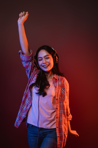 Azjatycka kobieta słuchająca muzyki ze słuchawkami uniosła ręce ciesząc się muzyką