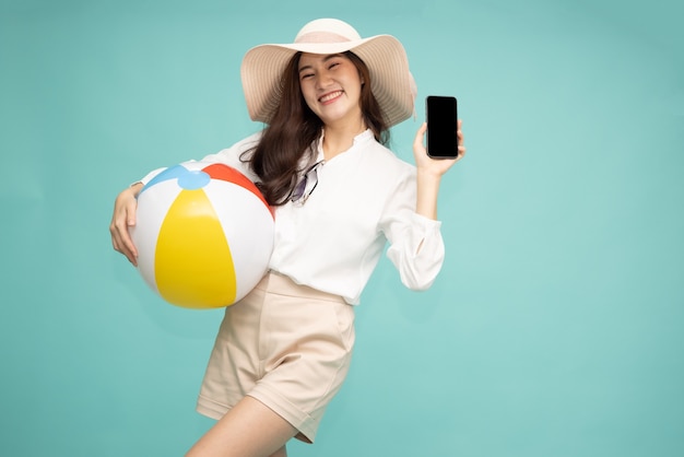 Azjatycka kobieta trzyma telefon komórkowy i piłkę plażową na białym tle na zielonym tle