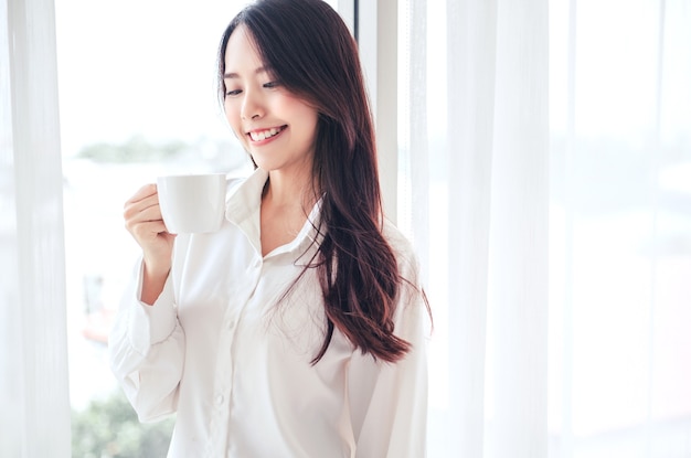 Azjatycka kobieta trzymając się za ręce filiżankę kawy rano