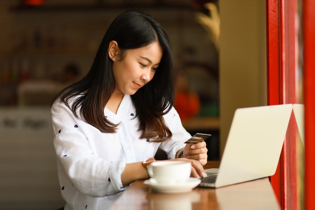 Azjatycka kobieta używa laptopu działanie i pije kawę w kawiarni