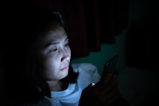 Azjatycka kobieta w nocy bawi się smartfonem w łóżkuTajlandczycy