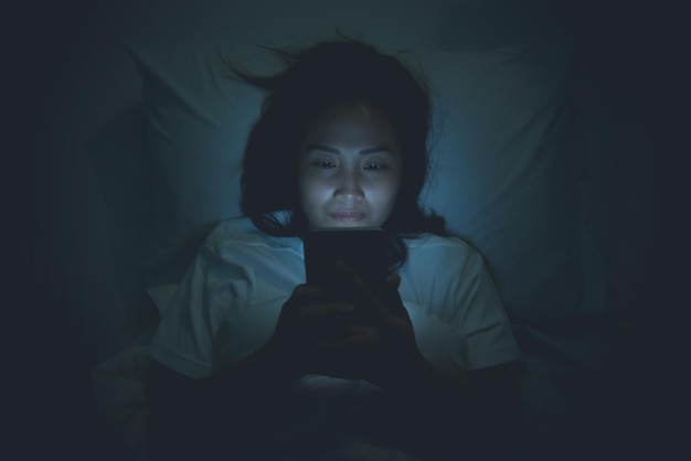 Azjatycka kobieta w nocy bawi się smartfonem w łóżkuTajlandczycy