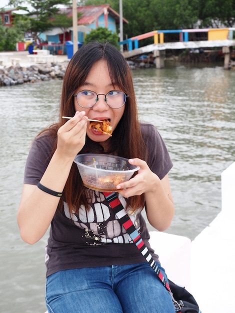 Azjatycka kobieta w okularach siedzi i je tajską przekąskę chrupiące smażone krewetki