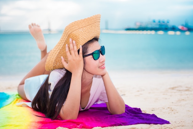 Azjatycka kobieta w przypadkowym i słomianym kapeluszu lying on the beach na tropikalnej plaży z dennym tłem