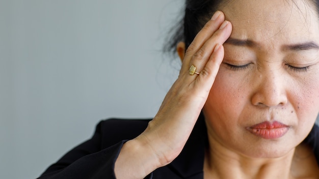 Azjatycka Kobieta W średnim Wieku, Starsza Kobieta Odczuwa Ból I Cierpi Na Nagły Ból Głowy Oraz Atak Udaru Mózgu I Trzyma Się Za Głowę Ze Zestresowaną Twarzą. Pojęcie Problemu Mózgu I Głowy.