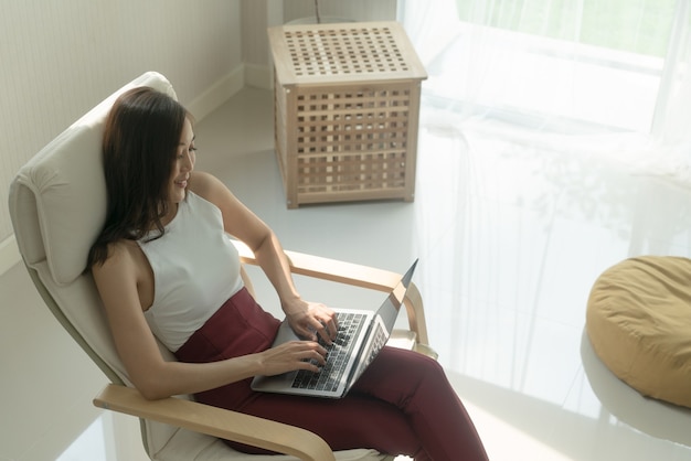 Zdjęcie azjatycka kobieta w swobodnym wyglądzie pracująca ze słuchawkami i laptopem notebook w salonie living