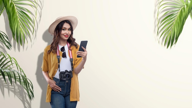 Azjatycka kobieta z kapeluszem i kamerą trzymająca telefon komórkowy w podróży