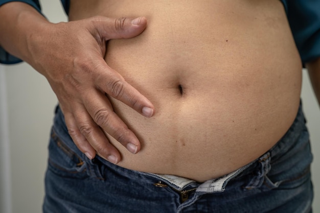 Azjatycka kobieta z nadwagą pokazuje gruby brzuch w biurze