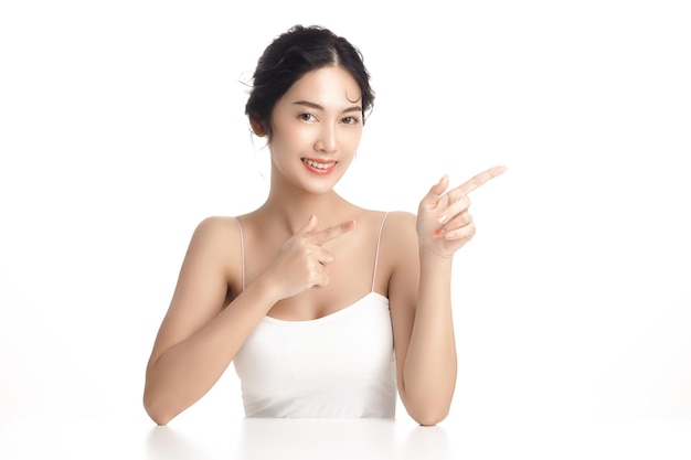 Azjatycka kobieta z piękną twarzą i idealnie czystą świeżą skórą Cute modelki wskazuje na wolne miejsce na białym tle na białym tle Zabieg na twarz Kosmetologia piękno koncepcja