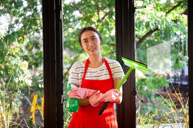 Azjatycka kobieta z pieluchy cleaning okno. Mycie szkła w oknach sprayem do czyszczenia.