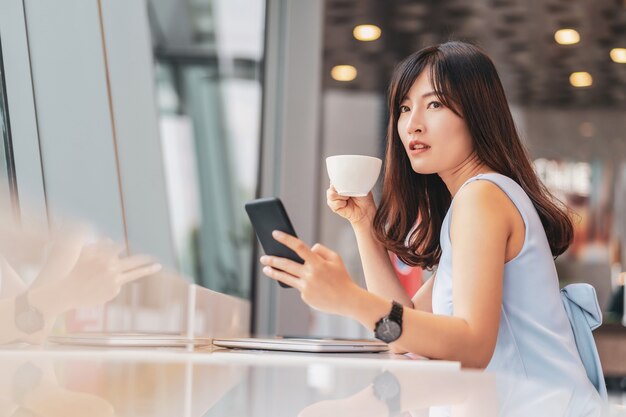 Azjatycka kobieta za pomocą inteligentnego telefonu komórkowego do zakupów online w nowoczesnej kawiarni