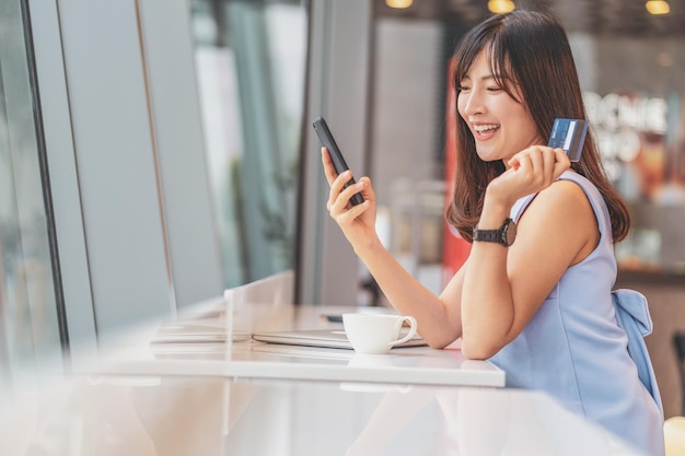 Azjatycka kobieta za pomocą karty kredytowej z telefonem komórkowym na zakupy online w nowoczesnej kawiarni,