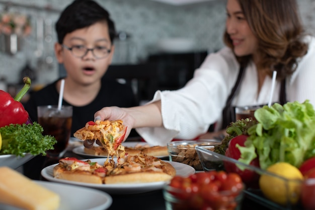 Azjatycka Mama I Syn Siedzą W Domowej Kuchni I Jedzą Domową Pizzę Razem Z Różnymi Rodzajami Warzyw. Pomysł Na Radość Z Spędzania Czasu W Rodzinie.