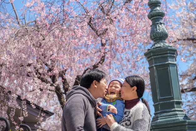 Azjatycka matka i ojciec całują syna malucha w wiosennym ogrodzie kwitnącym sakura lub kwiat wiśni