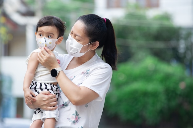 Azjatycka matka nosząca białą maskę trzyma swoją małą córeczkę, która jest jej córką, stara się dbać o swoje dziecko, nosząc maskę na twarz, koncepcja COVID-19