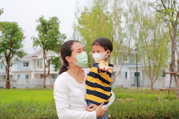 Azjatycka Matka Nosząca Syna W Masce Ochronnej Zarówno W Publicznym Ogrodzie Podczas Epidemii Koronawirusa, Jak I Grypy