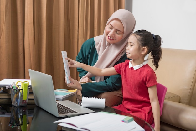 Azjatycka matka pomaga małej dziewczynce odrabianiu lekcji z laptopem w domu. Edukacja online podczas kwarantanny