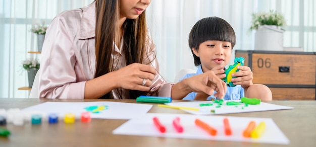 Azjatycka matka pracuje w domu razem z synem. Mama i dziecko bawią się ciastem. Dziecko tworząc model z gliny z plasteliny. Styl życia kobiety i aktywność rodzinna.