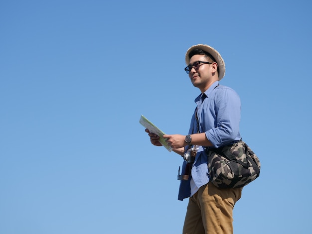 Azjatycka mężczyzna podróż z mapą i rocznik kamerą na niebieskiego nieba tle