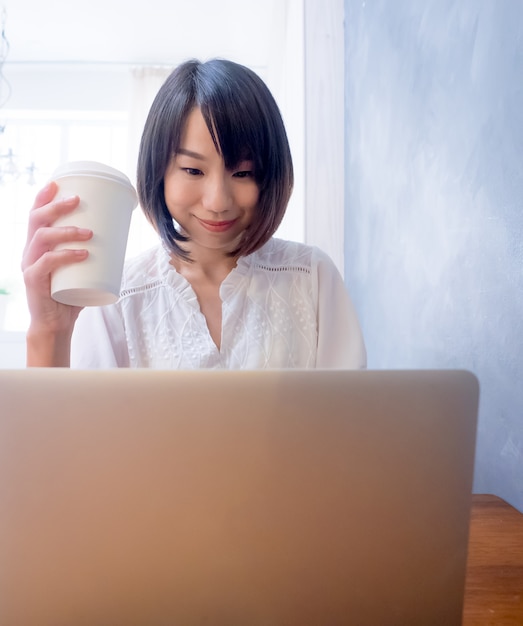 Azjatycka młoda kobieta pije przed laptopem