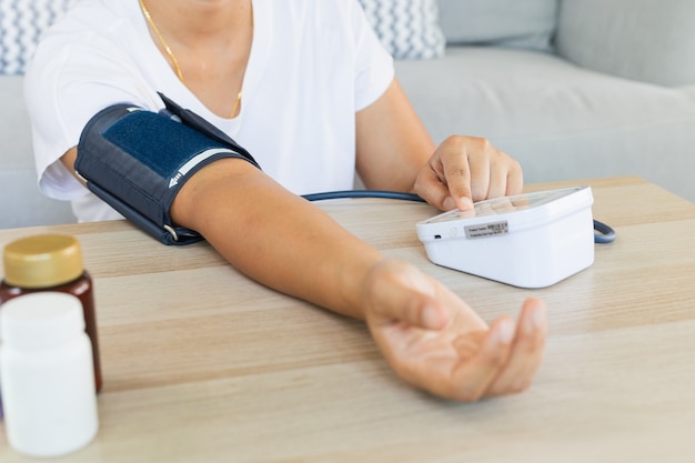 Azjatycka młoda kobieta samodzielnie w domu sprawdza ciśnienie krwi i tętno cyfrowym manometrem. Pojęcie zdrowia i medycyny.