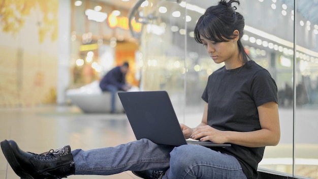 Azjatycka młoda kobieta siedzi na podłodze z laptopem w centrum handlowym w centrum handlowym