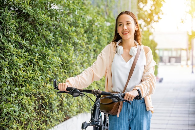 Azjatycka młoda kobieta spaceruje z rowerem latem w wiejskim parku na świeżym powietrzu Szczęśliwa uśmiechnięta kobieta spaceruje ulicą z rowerem po miejskiej drodze Środowisko ekologiczne zdrowe podróże wakacyjne