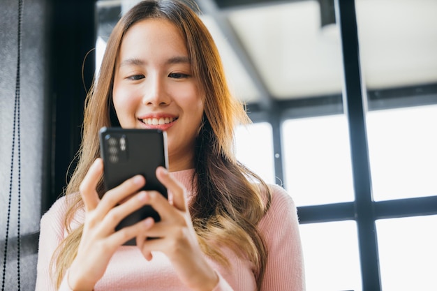 Azjatycka młoda kobieta trzymająca telefon komórkowy w kawiarni w kawiarni