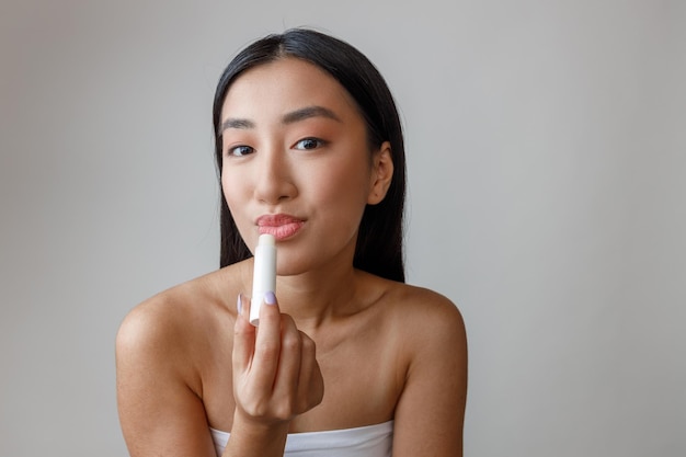 Azjatycka młoda kobieta używa higienicznej szminki w studio