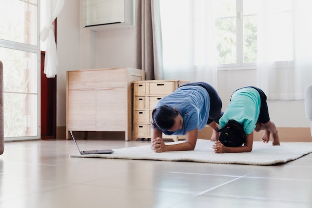 Azjatycka młoda matka i jej córka robi ćwiczenia rozciągające fitness jogi razem w domu. Rodzic uczący dziecko ćwiczy, aby być silnym i utrzymywać zdrowie fizyczne i dobre samopoczucie w codziennej rutynie.