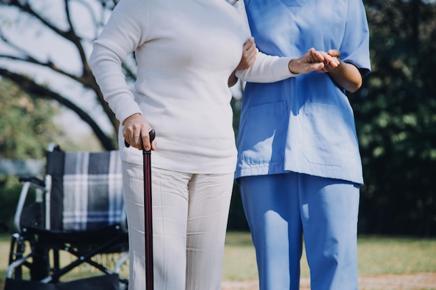 Azjatycka młoda opiekunka pielęgniarka wspiera starszego starszego mężczyznę spacerującego na świeżym powietrzu Specjalistyczna dziewczyna lekarz pomaga i opiekuje się starszym dojrzałym mężczyzną pacjentem wykonującym fizykoterapię w publicznym parku w domu opieki