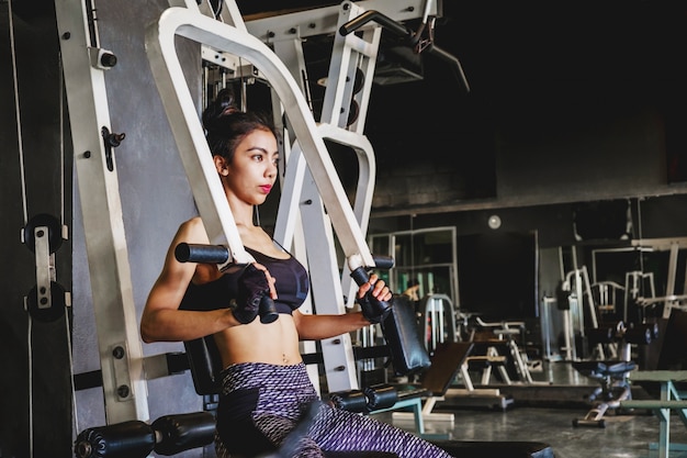 Azjatycka młoda sprawności fizycznej kobieta wykonuje ćwiczenie z maszyną do ćwiczeń w gym