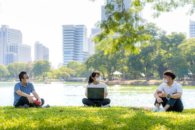 Azjatycka młoda trójka mężczyzna i kobieta rozmawiają i relaksują się z przyjacielem i noszą maskę w odległości do 6 stóp, chronią przed wirusami COVID-19 w celu zdystansowania się
