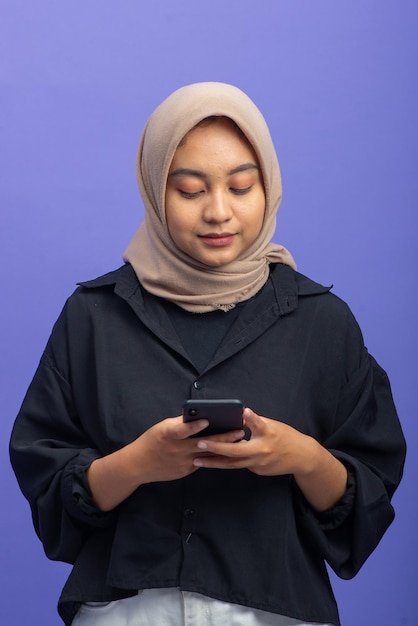 Azjatycka muzułmanka trzymając telefon komórkowy na białym tle na fioletowym tle