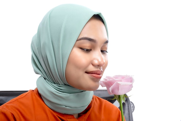 Azjatycka muzułmanka w chustce siedzi w walizce trzymając różowy kwiat róży