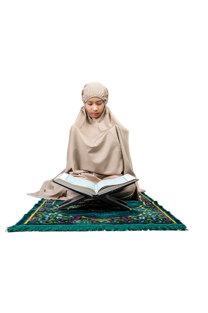 Azjatycka muzułmańska dziewczyna w hidżabie z Koranem na dywaniku modlitewnym podniosła ręce i modliła się