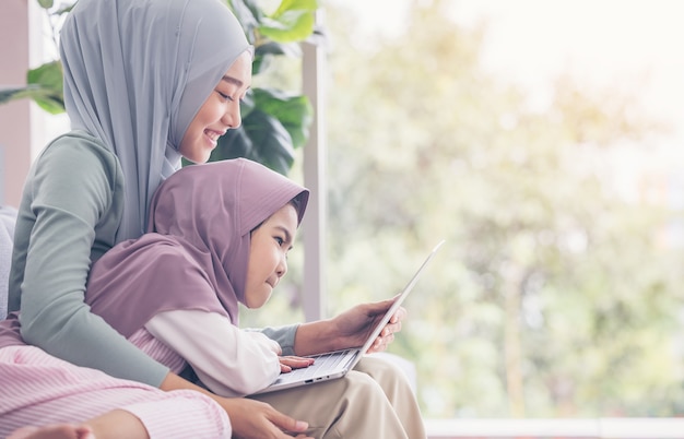 Azjatycka muzułmańska matka i córka uśmiecha się podczas korzystania z laptopa razem