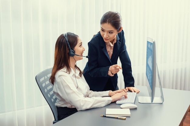 Azjatycka operatorka obsługi klienta nosząca zestaw słuchawkowy jest prowadzona przez swojego wspierającego menedżera Doświadczony współpracownik pomaga operatorowi obsłużyć połączenie z klientem, udzielając porad i wskazówek Entuzjastycznie