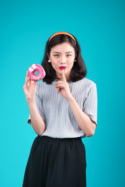 Azjatycka piękna dziewczyna gospodarstwa różowy pączek. Retro radosna kobieta ze słodyczami, deser stojący na niebieskim tle.